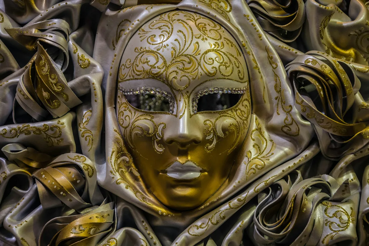 A gold and white masquerade-style mask with bejewelled trim